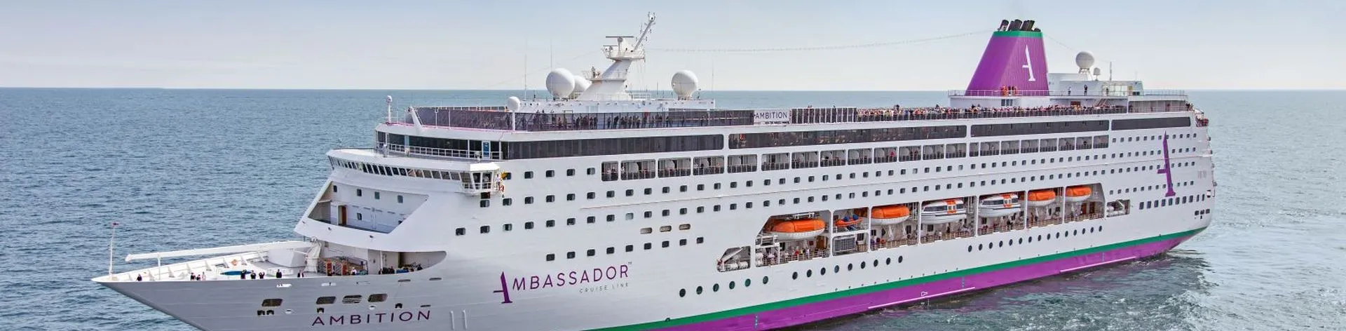 A large contemporary cruise ship navigates open ocean waters under clear skies. The vessel features multiple decks, a distinctive funnel, and modern design typical of mid-to-large sized cruise liners built in the 2000s-2010s era.