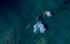 An breathtaking aerial perspective of a pristine tropical island surrounded by crystal-clear turquoise waters, with a small boat visible near the shore. The image captures the natural beauty and remote isolation typical of exclusive cruise destination islands in the Caribbean region.