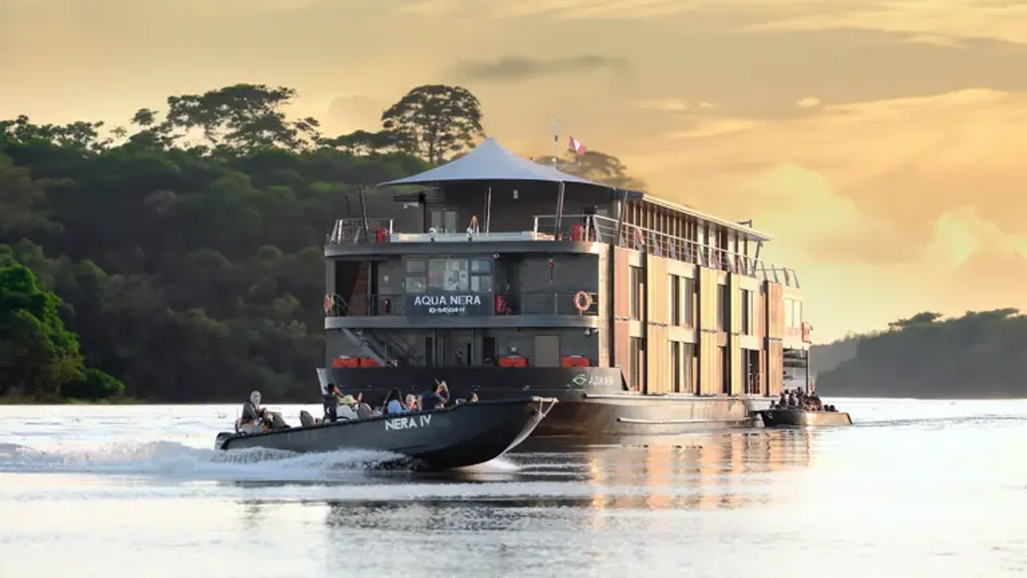 Amazon River Cruise Vessel at Sunset A luxury river cruise ship named Aqua Nera navigating through a lush Amazon rainforest landscape during a golden sunset. The vessel is accompanied by smaller boats and features multiple decks with panoramic windows.