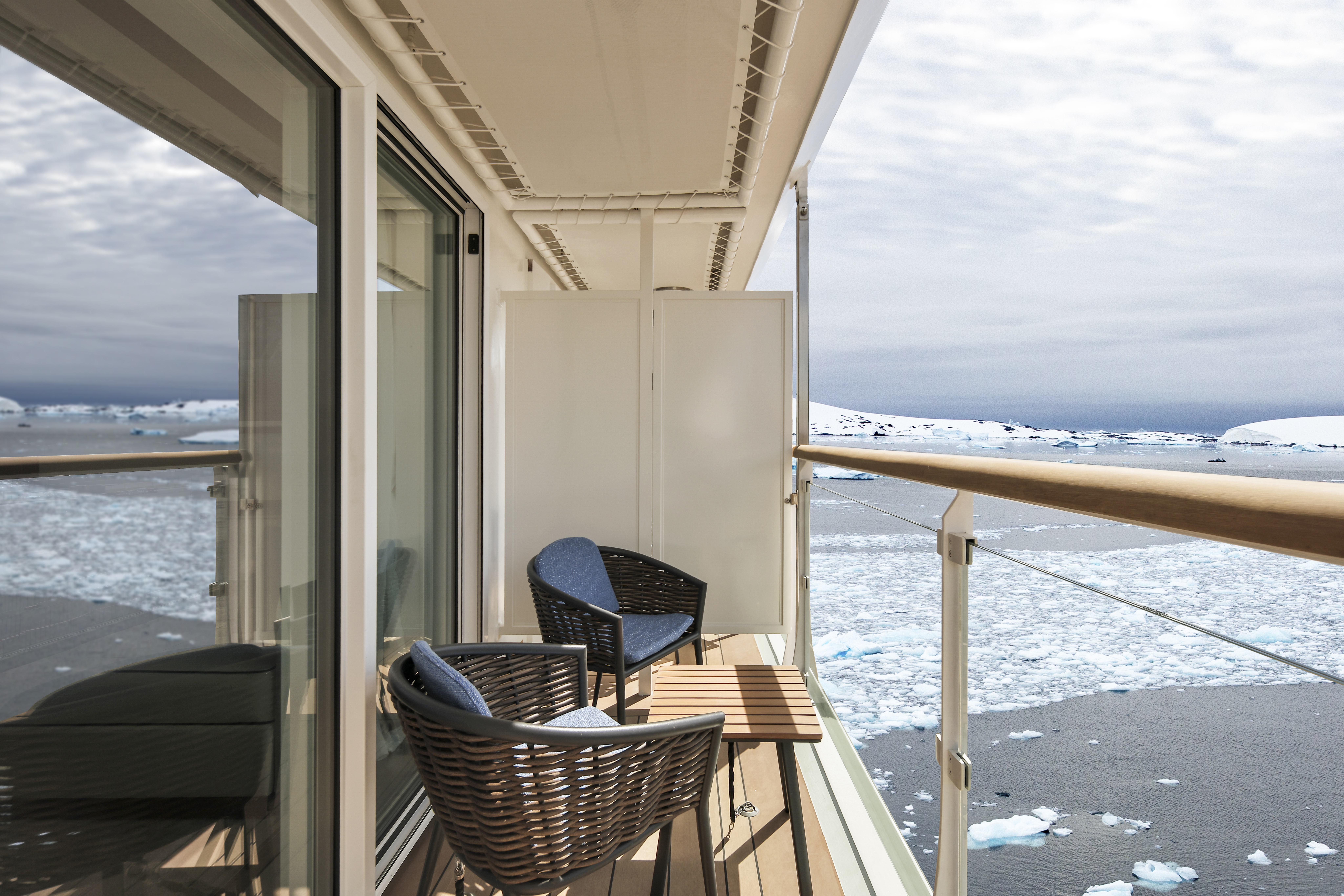 Arctic Cruise Balcony with Icy Seascape A private balcony on a cruise ship featuring woven chairs overlooking a frozen, ice-filled polar seascape with snowy landscapes in the background. The balcony offers a serene view of a stark, white and blue Arctic environment.