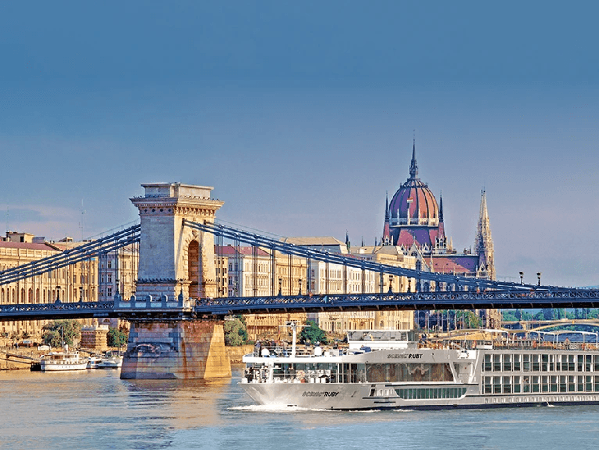 Budapest Chain Bridge and Parliament A scenic view of the iconic Chain Bridge spanning the Danube River with the Hungarian Parliament building in the background, featuring a river cruise ship in the foreground.