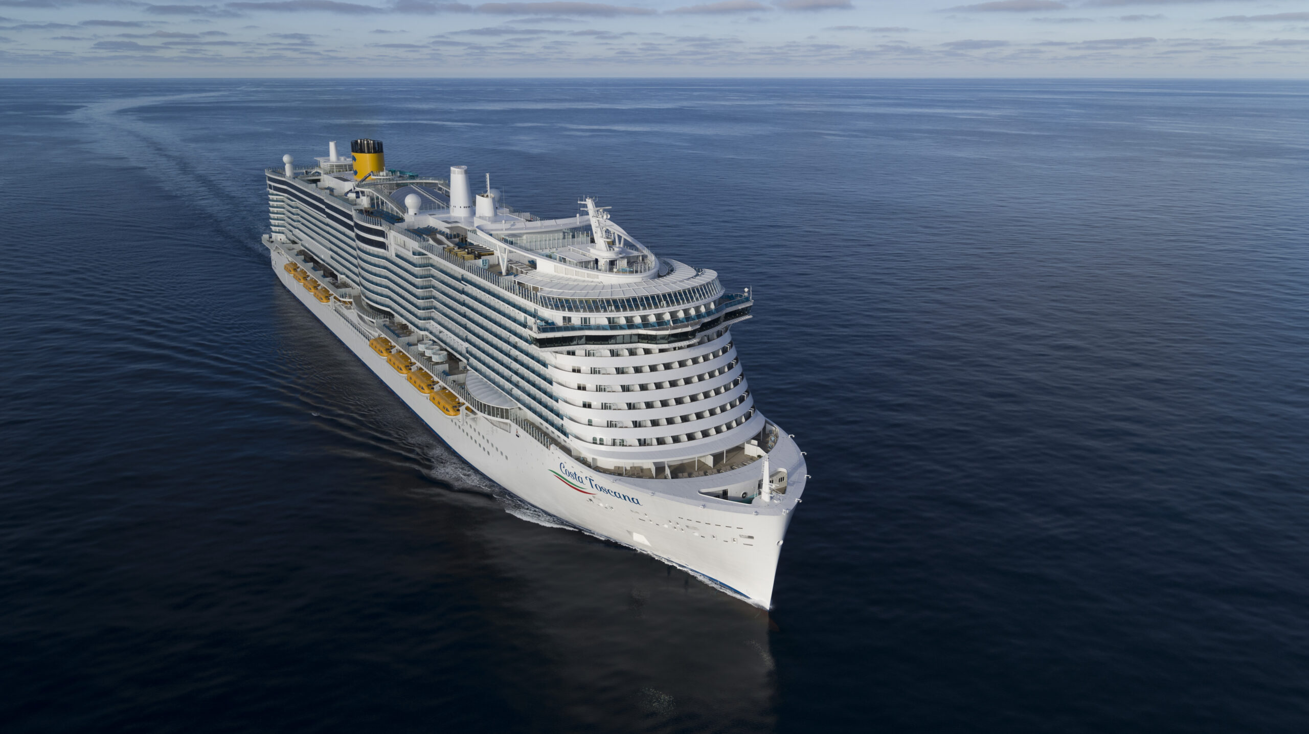 Cruise Ship Sailing on Calm Blue Ocean A large white cruise ship with yellow and white color scheme sailing across a serene, flat blue ocean under an overcast sky. The vessel appears to be a modern, sleek cruise liner with multiple decks and balconies.