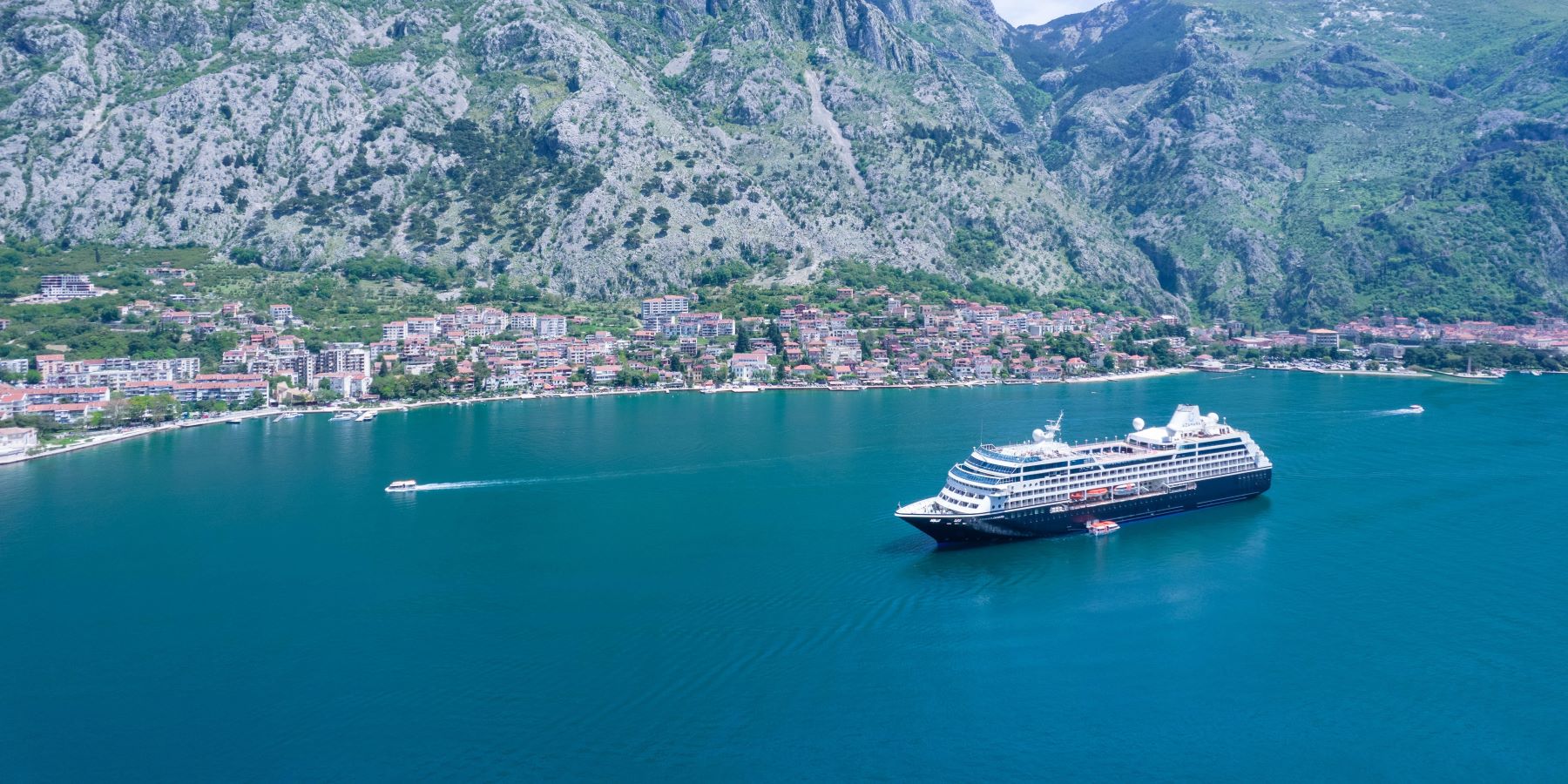 Cruise Ship in Coastal Mountain Landscape A large cruise ship anchored in a turquoise bay surrounded by steep, rocky mountains with