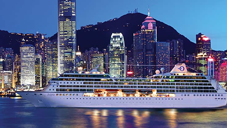 Cruise Ship in Hong Kong Harbor at Night A large white cruise ship docked in Victoria Harbor with the illuminated Hong Kong skyline in the background, featuring skyscrapers and mountains at twilight.