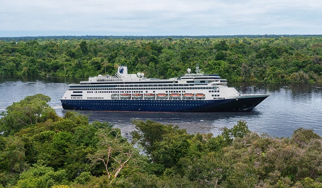 Cruise Ship in Lush Tropical Waterway A dark blue and white cruise ship navigating through a narrow river surrounded by dense, green tropical forest. The vessel appears to be mid-journey through a verdant landscape with water and trees on both sides.