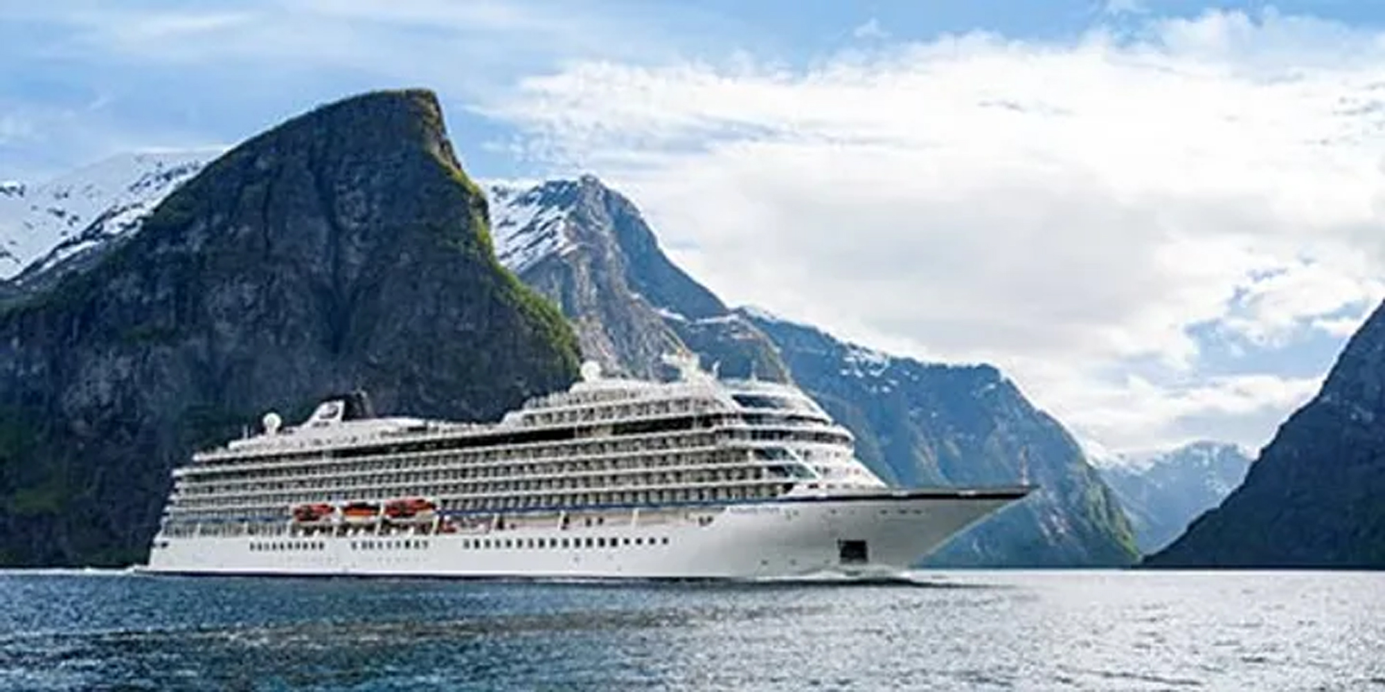 Cruise Ship in Majestic Fjord Landscape A large white cruise ship sailing through a stunning fjord with steep, snow-capped mountains on either side. The scenic landscape features dramatic rocky cliffs and blue waters under a partly cloudy sky.
