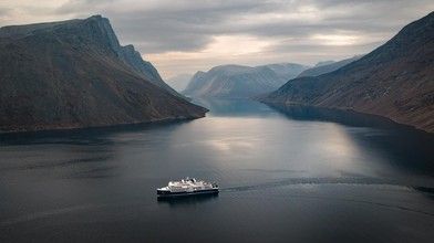 Cruise Ship in Norwegian Fjord A passenger cruise ship navigates through a dramatic Norwegian fjord surrounded by steep mountain cliffs and calm blue waters under an overcast sky. The majestic landscape showcases the natural beauty of Scandinavia with towering peaks reflected in the still water.