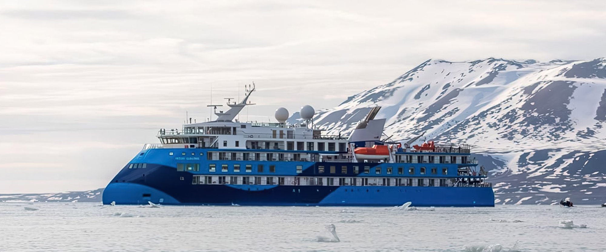 Expedition Cruise Ship in Arctic Waters A modern blue expedition cruise ship navigates Arctic waters alongside snow-covered mountains