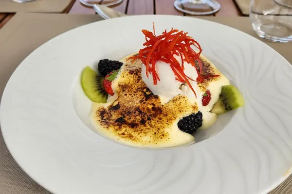 Fine Dining Dessert Presentation with Fresh Fruits An elegantly plated fine dining dessert featuring a creamy custard or mousse base topped with fresh kiwi and blackberries, dusted with golden spice powder, garnished with delicate red chili strands, and a quenelle of white cream. The presentation exemplifies the sophisticated culinary offerings found in premium cruise ship dining venues.