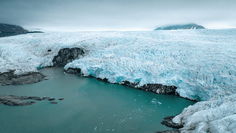 Glacial Lagoon with Turquoise Waters A stunning Arctic glacier descends steeply to meet turquoise glacial meltwater, with ice cliffs towering above rocky shores and mountains visible in the misty background. The striking contrast between brilliant blue ice, white snow, and the vibrant turquoise water showcases the raw beauty of a polar ice landscape, likely in Svalbard or similar Arctic destination.