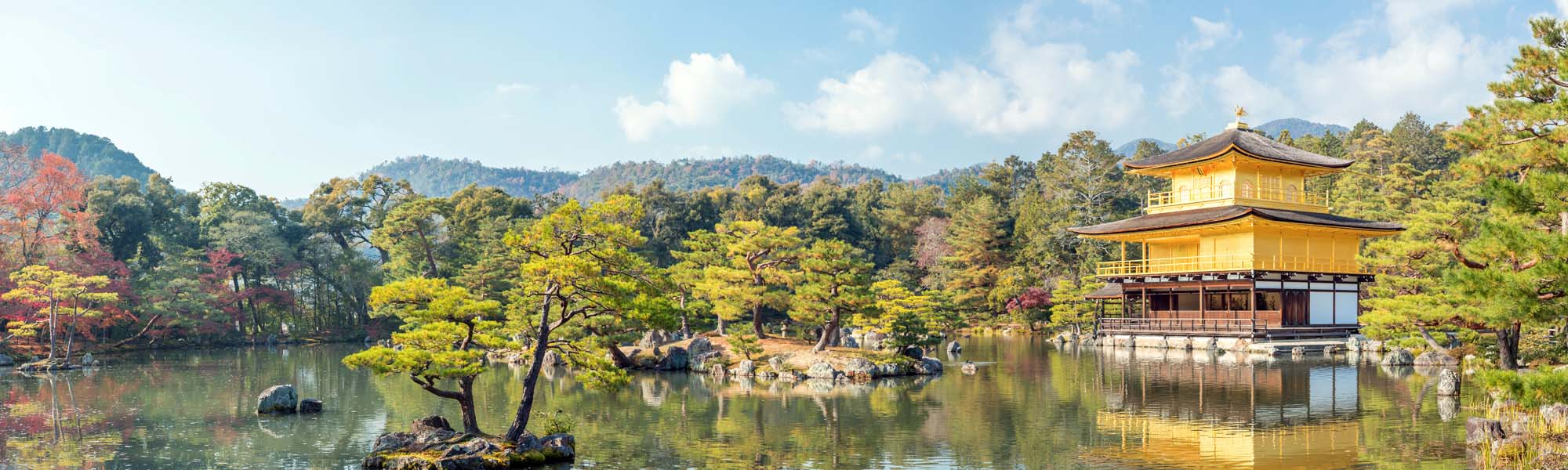 Golden Pavilion at Kyoto’s Kinkaku-ji Temple A serene landscape featuring the iconic gold-leaf covered Kinkaku-ji (Golden Pavilion) set against a tranquil pond with pine trees and mountains in the background. The pavilion reflects perfectly in the still water, creating a mesmerizing scene of Japanese architectural beauty.