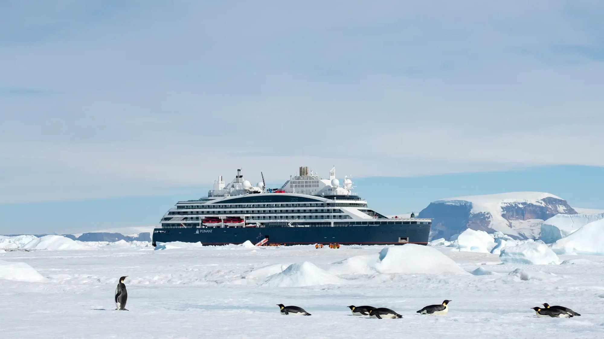 Luxury Cruise Ship in Antarctic Landscape A sleek, modern cruise ship navigates through calm waters with rugged mountain terrain in the background. The vessel is adorned with multiple satellite domes and has a clean, contemporary design.