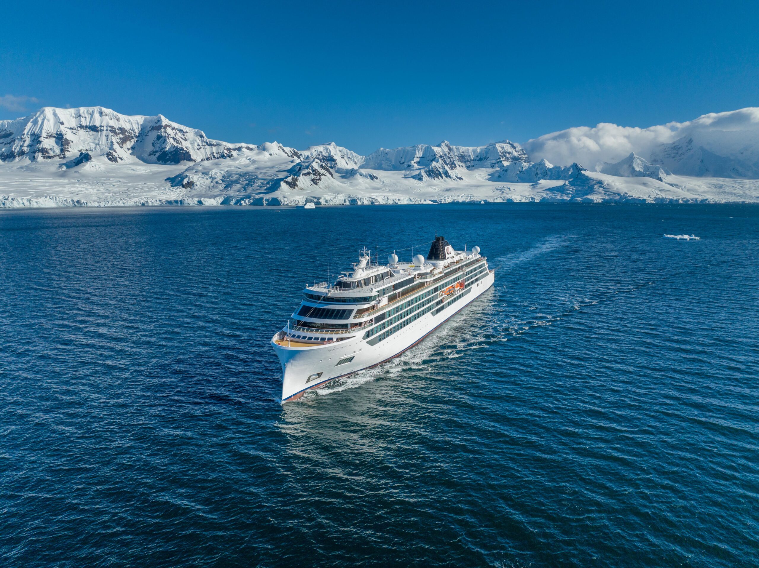 Luxury Cruise Ship in Antarctic Waters A white cruise ship sailing through deep blue waters with a dramatic snow-covered mountain and glacier landscape in the background. The vessel appears to be navigating through the pristine polar region.