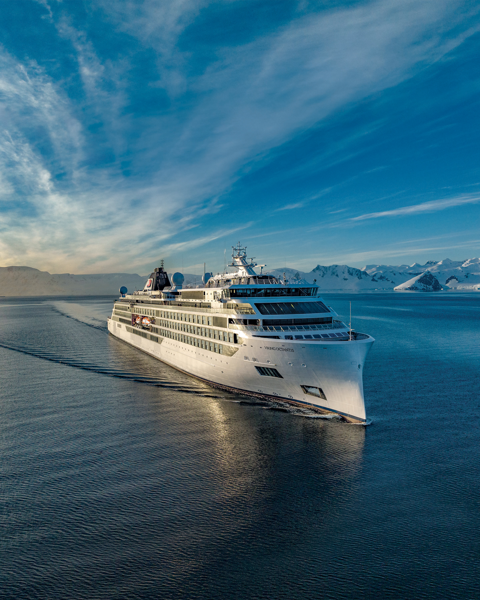 Luxury Cruise Ship in Arctic Landscape A pristine white cruise ship sailing through calm blue waters with snow-capped mountains and glacial landscape in the background under a dramatic sky.