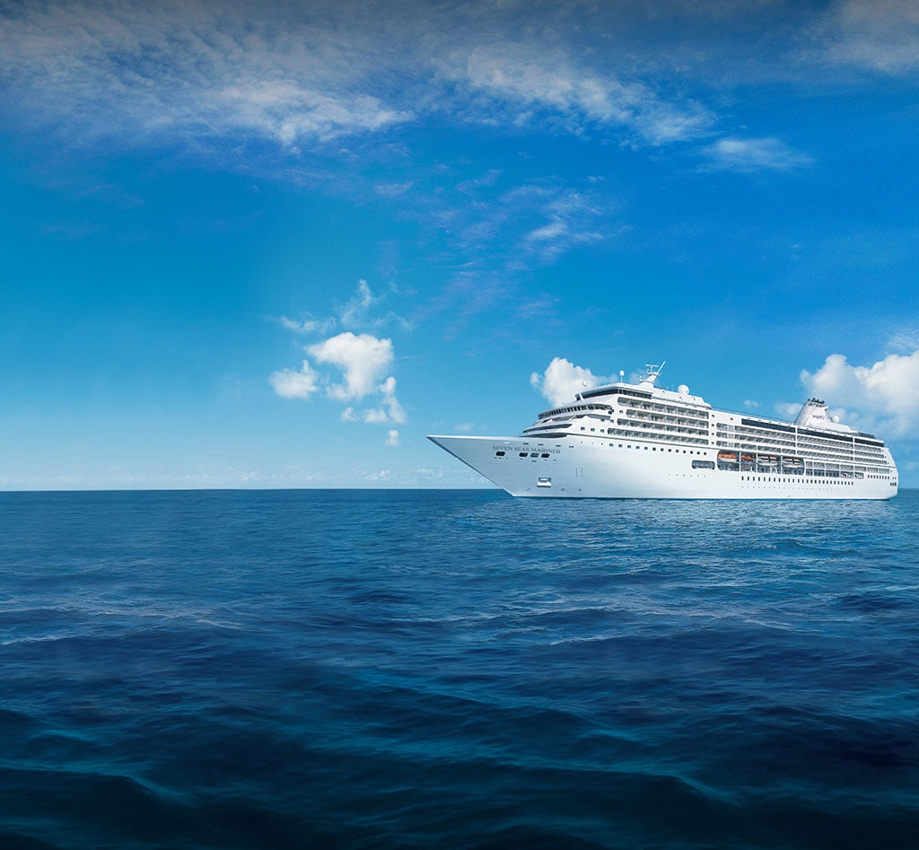 A pristine white cruise ship sailing on deep blue waters under a clear sky with scattered white clouds. The vessel appears large and elegant, representing modern maritime travel.