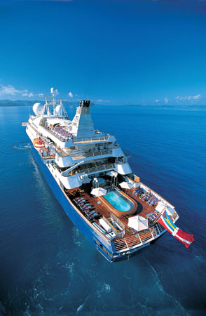 Luxury Cruise Ship on Turquoise Waters An aerial view of a pristine white cruise ship sailing on crystal blue waters, featuring multiple decks, a swimming pool, and expansive outdoor spaces.