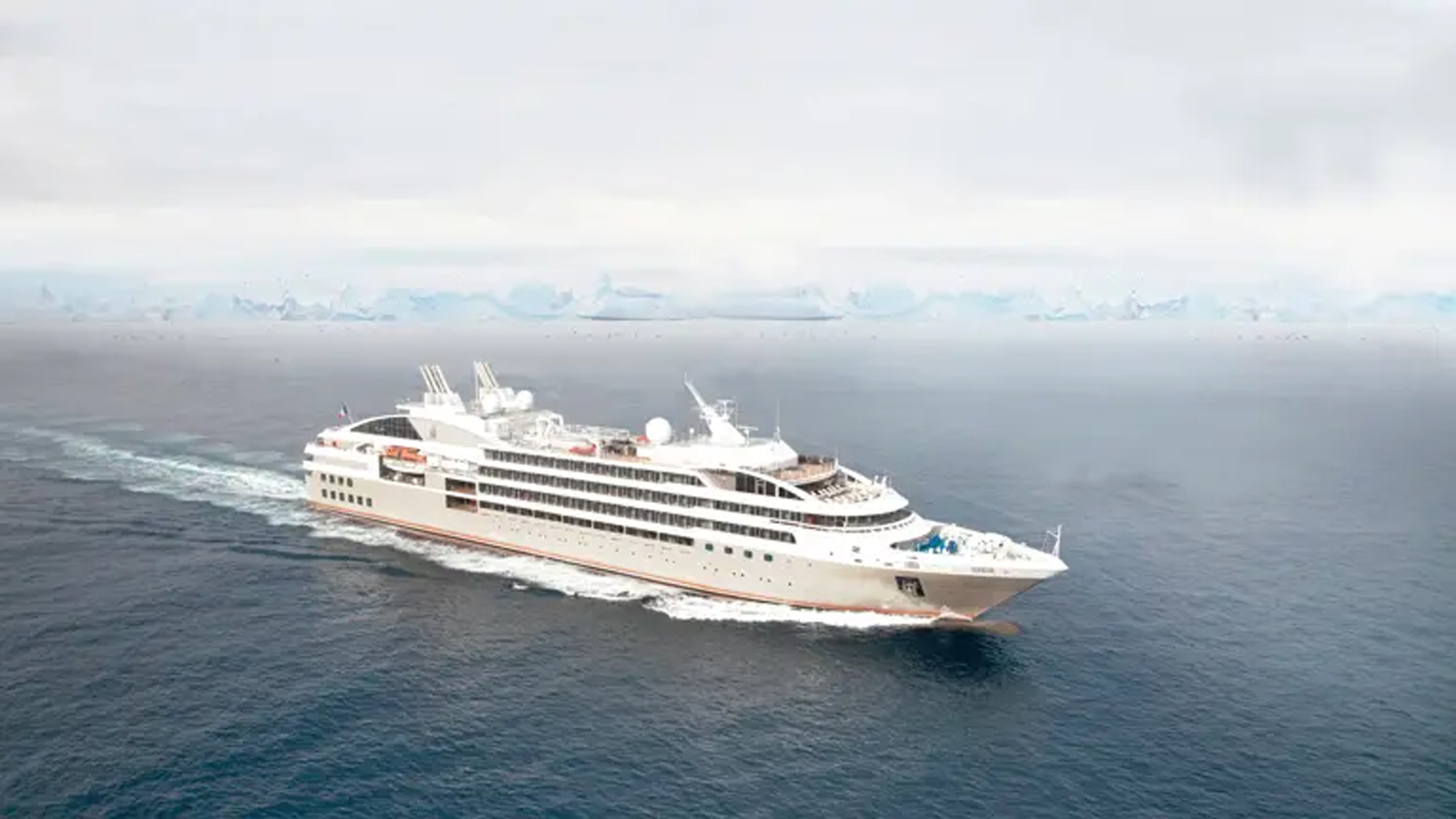 Luxury Expedition Cruise Ship in Polar Regions A sleek white expedition cruise ship navigating through cold, misty waters with an icy horizon in the background. The vessel appears designed for polar or arctic exploration.