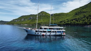 Luxury Gulet Cruise in Mediterranean Waters A striking two-masted luxury gulet sailing vessel anchors in crystal-clear turquoise waters surrounded by lush, forested mountains. The elegant white yacht, equipped with multiple decks and modern amenities, exemplifies Mediterranean cruise tourism in a pristine natural setting.