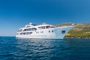 Luxury Motor Yacht Anchored in Mediterranean Waters A pristine white motor yacht with multiple decks anchored in crystal-clear turquoise waters near a rocky Mediterranean coastline. The vessel features elegant white architecture with multiple levels and contemporary design, perfect for luxury cruising and private charter experiences.