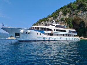 Luxury Motor Yacht Anchored in Mediterranean Waters A sleek, modern motor yacht with multiple decks and white hull anchors in crystal-clear turquoise waters beside a dramatic rocky coastline, showcasing luxury cruise and yacht charter experiences in Mediterranean destinations.