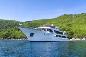 Luxury Motor Yacht Anchored in Tropical Waters A sophisticated white multi-deck motor yacht is anchored in crystal-clear turquoise waters adjacent to lush, verdant hillsides. The vessel appears to be a high-end expedition or charter yacht, showcasing modern nautical design with multiple decks and professional maritime features, ideal for luxury cruising and exploration in tropical destinations.