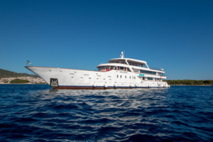 Luxury Motor Yacht in Mediterranean Waters A white luxury motor yacht anchored in crystal-clear blue Mediterranean waters under a clear sky. The vessel features elegant white superstructure with red/orange accents and appears to be a mid-sized expedition or cruise yacht suitable for upscale yacht tourism and destination cruising.