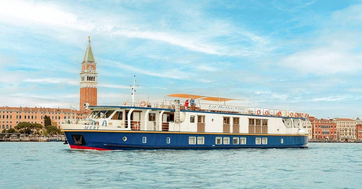 Luxury River Cruise Boat in Venice A modern luxury river cruise vessel named 'Mery' navigates the turquoise waters of the Grand Canal in Venice, Italy, with the iconic Campanile di San Marco bell tower prominently visible in the background amid traditional Venetian architecture.