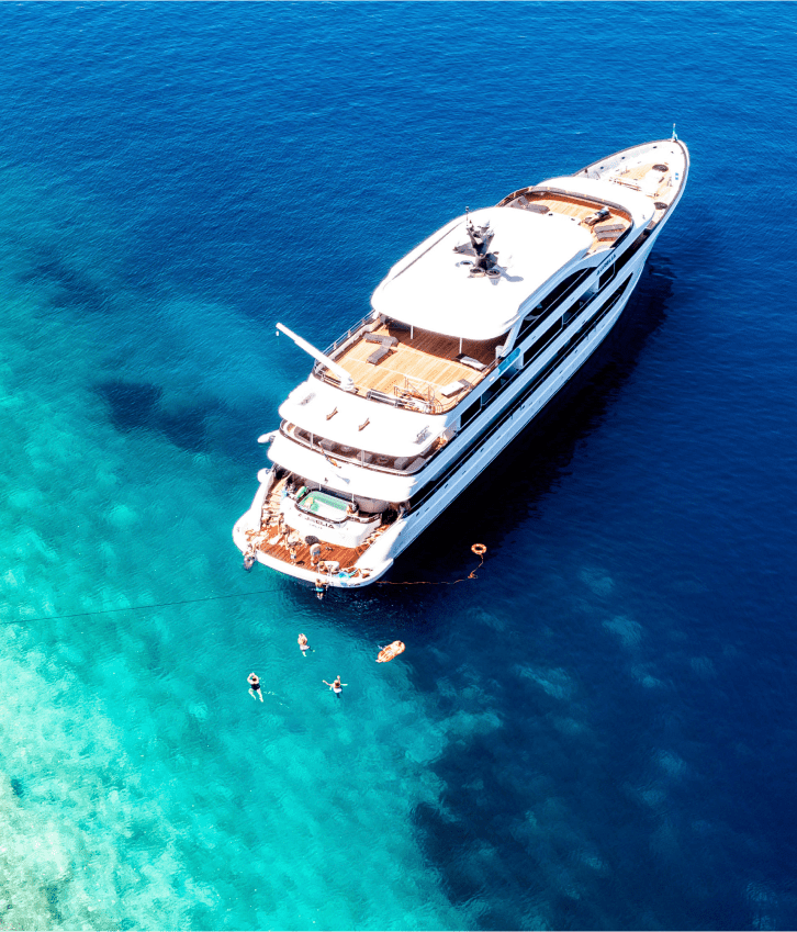Luxury Yacht Anchored in Turquoise Waters An aerial view of a multi-deck luxury motor yacht anchored in crystal-clear turquoise Mediterranean waters, with several guests swimming and enjoying water activities around the vessel.