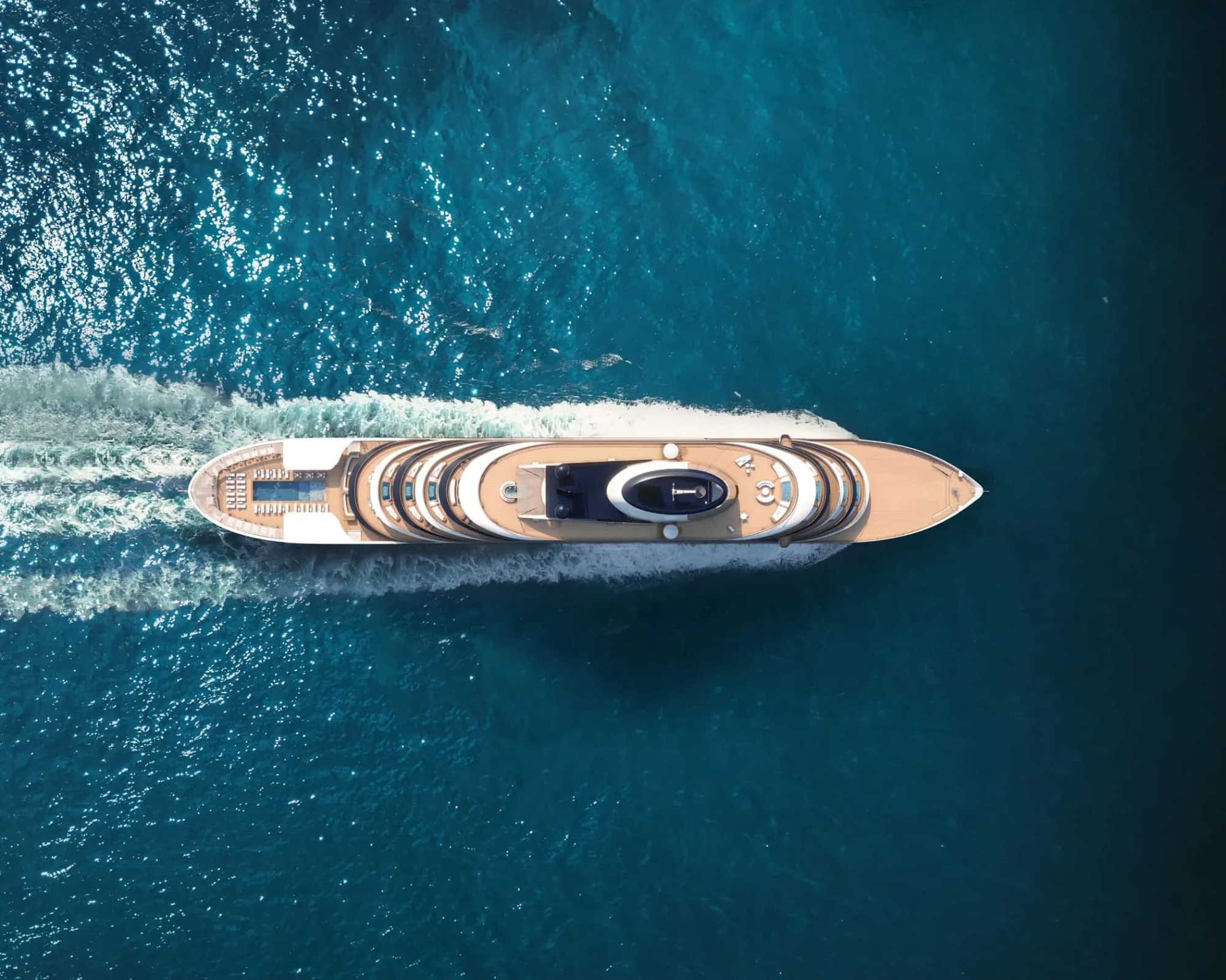 An aerial view of a sleek, modern luxury yacht cutting through deep blue ocean waters, showcasing its elegant multi-tiered design and smooth movement.