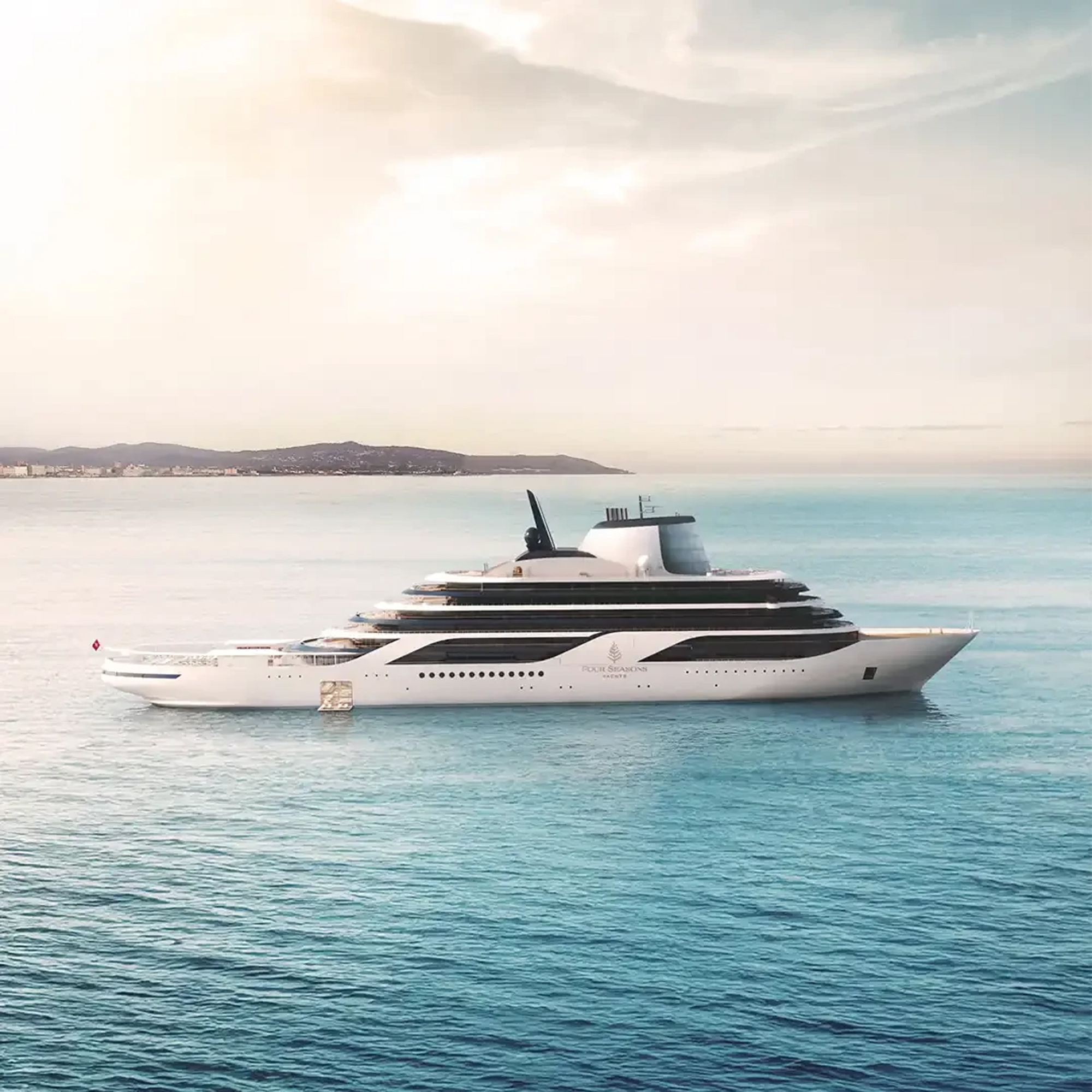 A sleek, modern white and grey luxury yacht sailing on calm turquoise waters with a coastline and hills visible in the background during soft daylight.
