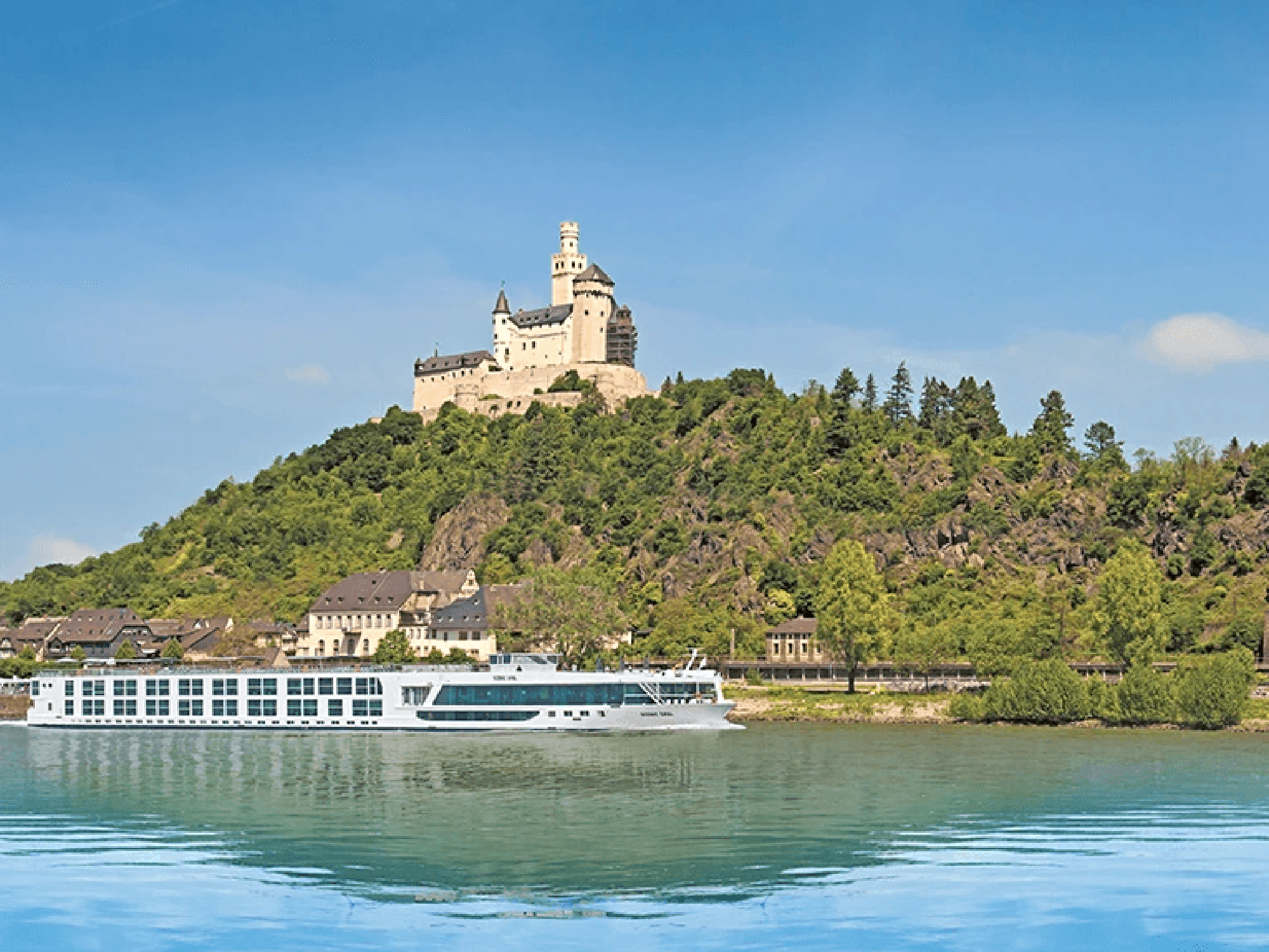 Marksburg Castle on the Rhine River A majestic medieval castle perched atop a forested hill overlooking the Rhine River, with a modern river cruise ship in the foreground. The scene captures the historic and scenic beauty of the Rhine Valley in Germany.