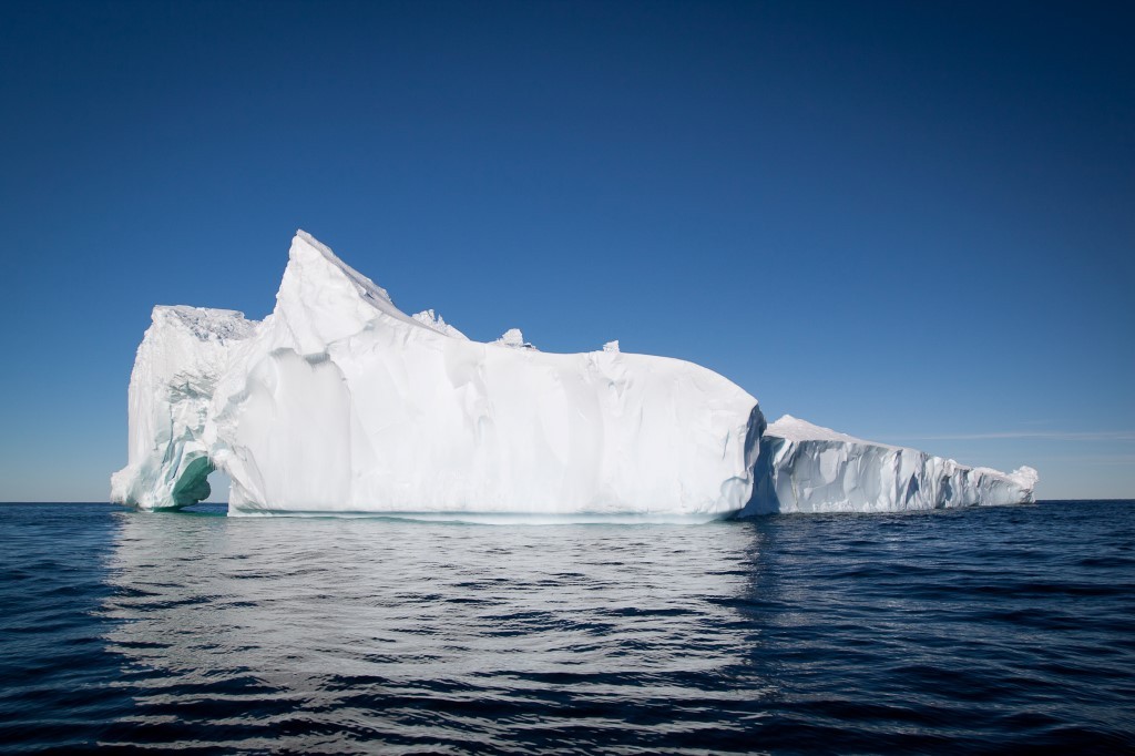 Massive Iceberg Floating in Arctic Waters A large, sculptural iceberg with brilliant white peaks and turquoise-tinted crevices floats in deep blue ocean waters under clear skies. The iceberg's dramatic jagged formations and towering profile showcase the raw beauty of polar regions, making it an iconic destination for Arctic cruise expeditions.