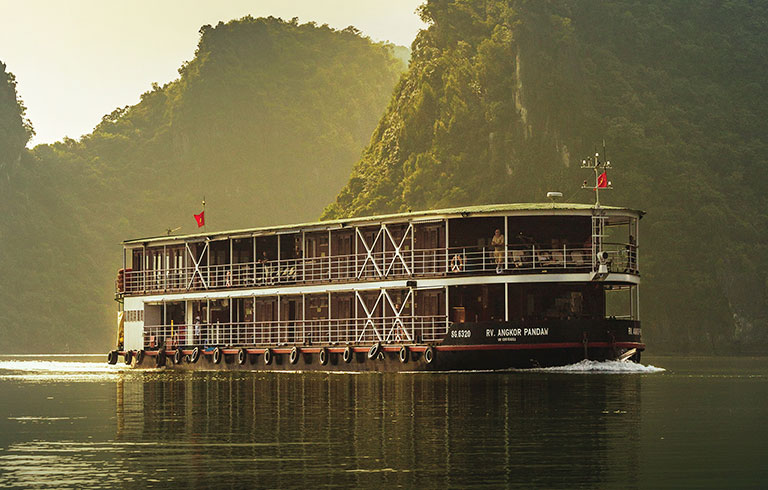 River Cruise Boat in Misty Mountain Landscape A multi-level river cruise boat navigating through a scenic landscape with lush green mountains and misty morning light. The vessel appears to be a river cruise ship sailing on a tranquil waterway.
