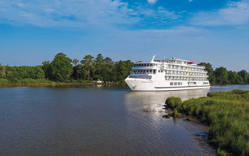 River Cruise Ship on Scenic Waterway A white river cruise vessel sailing through a serene waterway with lush green trees and grassy shorelines. The ship appears to be a modern, multi-deck river cruise ship navigating a calm, narrow river.