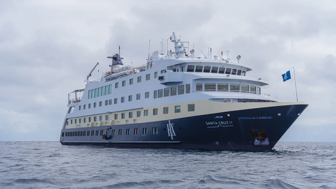 A sleek white and navy blue expedition cruise ship sailing on a gray, overcast ocean. The vessel appears to be a small to mid-sized expedition-style ship designed for adventure travel.