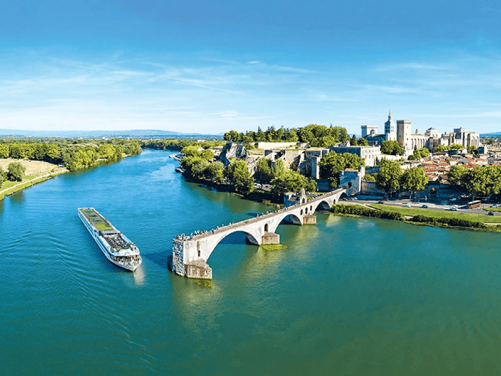 Scenic River Cruise in Avignon, France A river cruise ship passes by the historic Pont Saint-Bénézet (Pont d'Avignon) with the medieval city of Avignon and its famous papal palace in the background.