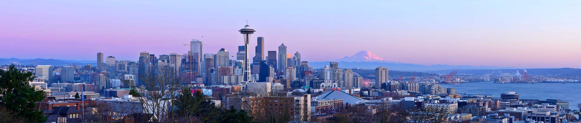 Seattle Skyline with Mount Rainier at Sunset A panoramic view of Seattle's downtown skyline featuring the iconic Space Needle, with Mount Rainier in the background during a pastel-colored twilight hour. The cityscape showcases modern skyscrapers, urban buildings, and the waterfront.