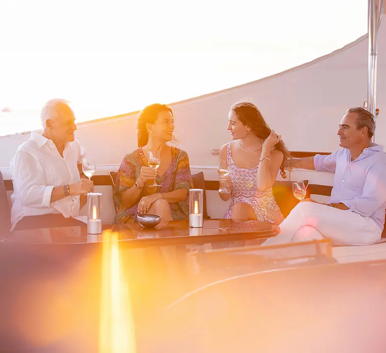Sunset Cocktail Hour on Cruise Ship Deck Four well-dressed guests enjoy cocktails and conversation on an upper deck of a cruise ship during golden hour, with the ocean and sunset sky visible in the background. The warm, golden lighting and relaxed atmosphere capture the luxury leisure experience of cruise travel.