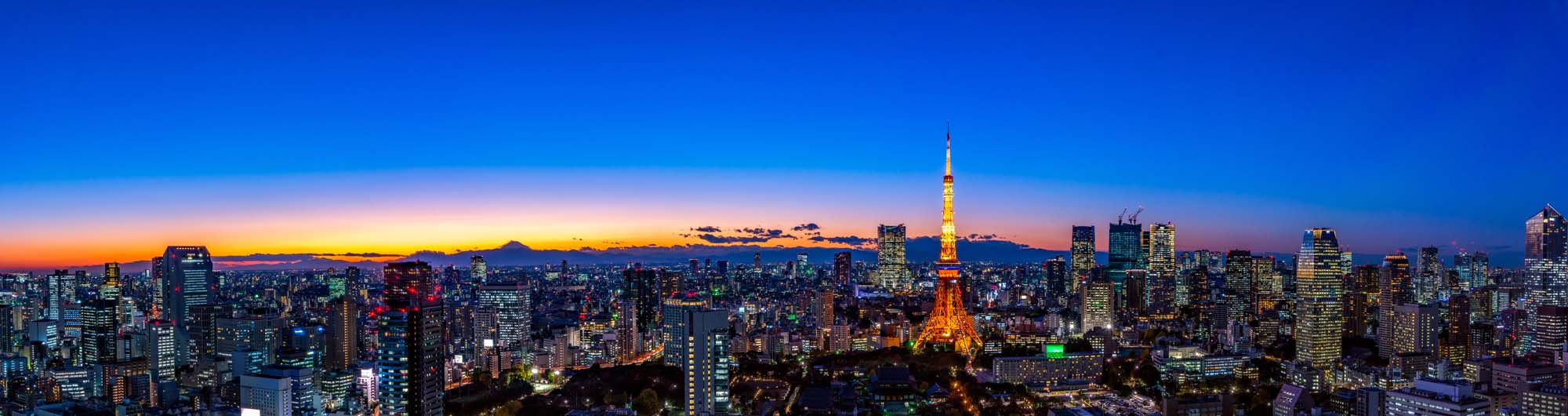 Tokyo Skyline at Twilight with Tokyo Tower A breathtaking panoramic view of Tokyo's urban landscape at sunset, featuring the iconic Tokyo Tower illuminated against a gradient sky with Mount Fuji in the distant background.