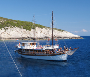 Traditional Gulet Sailing Boat in Mediterranean A classic wooden gulet sailing vessel anchored in crystal-clear turquoise Mediterranean waters, with white chalk cliffs visible in the background under clear blue skies. The traditional two-masted wooden boat features characteristic red and white hull coloring and is typical of Mediterranean coastal cruising experiences.