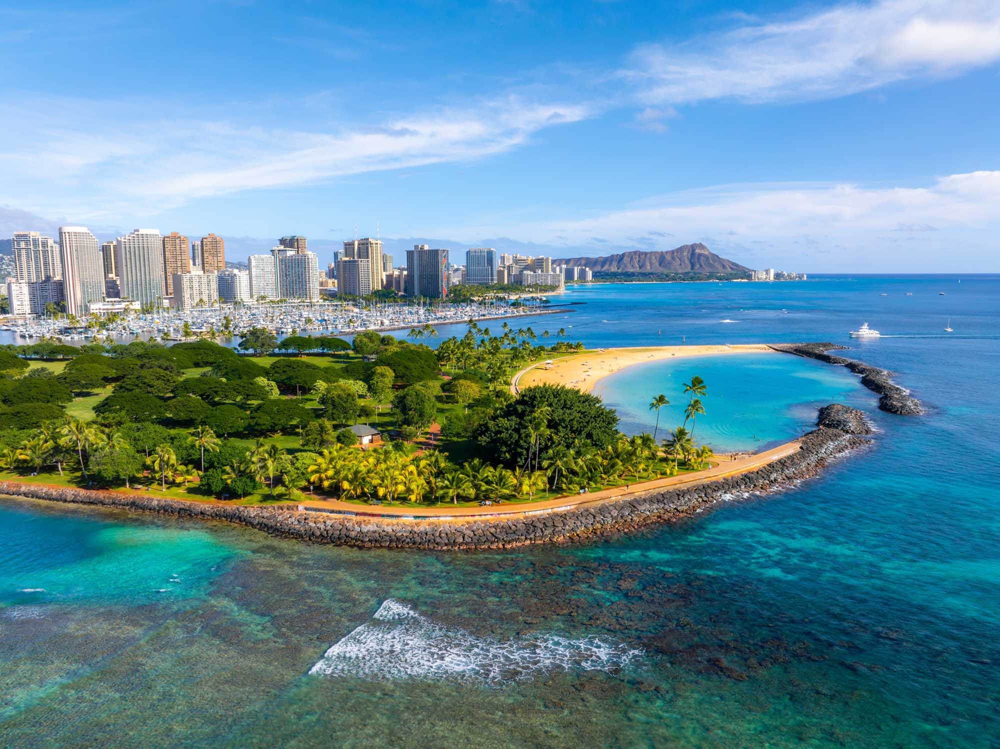 Aerial View of Honolulu with Diamond Head A stunning aerial photograph of Honolulu, Oahu, Hawaii, showcasing the iconic Diamond Head crater, vibrant turquoise waters, sandy beach, lush green park with palm trees, and the modern urban skyline of high-rise buildings. The image captures the perfect blend of natural beauty and urban development that defines Hawaii's capital city.