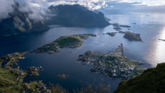 Arctic Fjord Archipelago Aerial View An aerial perspective of a stunning Arctic fjord landscape featuring deep blue waters dotted with small islands and rocky outcrops, surrounded by snow-capped mountains and dramatic cloud formations, characteristic of Nordic Arctic regions.