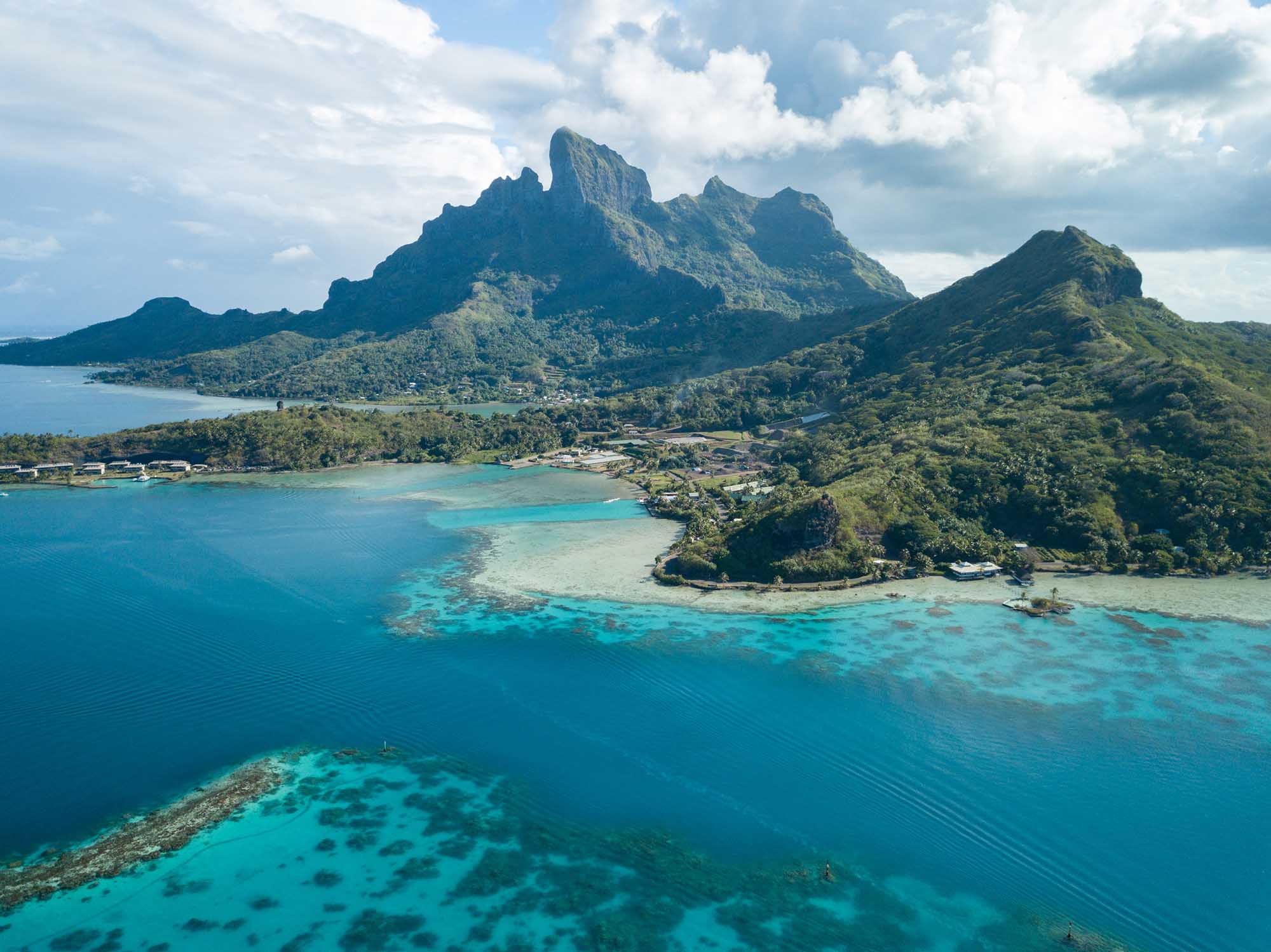 Bora Bora Aerial View with Mount Otemanu An aerial drone photograph of Bora Bora island in French Polynesia, featuring the iconic Mount Otemanu rising dramatically from lush tropical vegetation, surrounded by stunning turquoise lagoon waters and coral reefs visible beneath the surface.