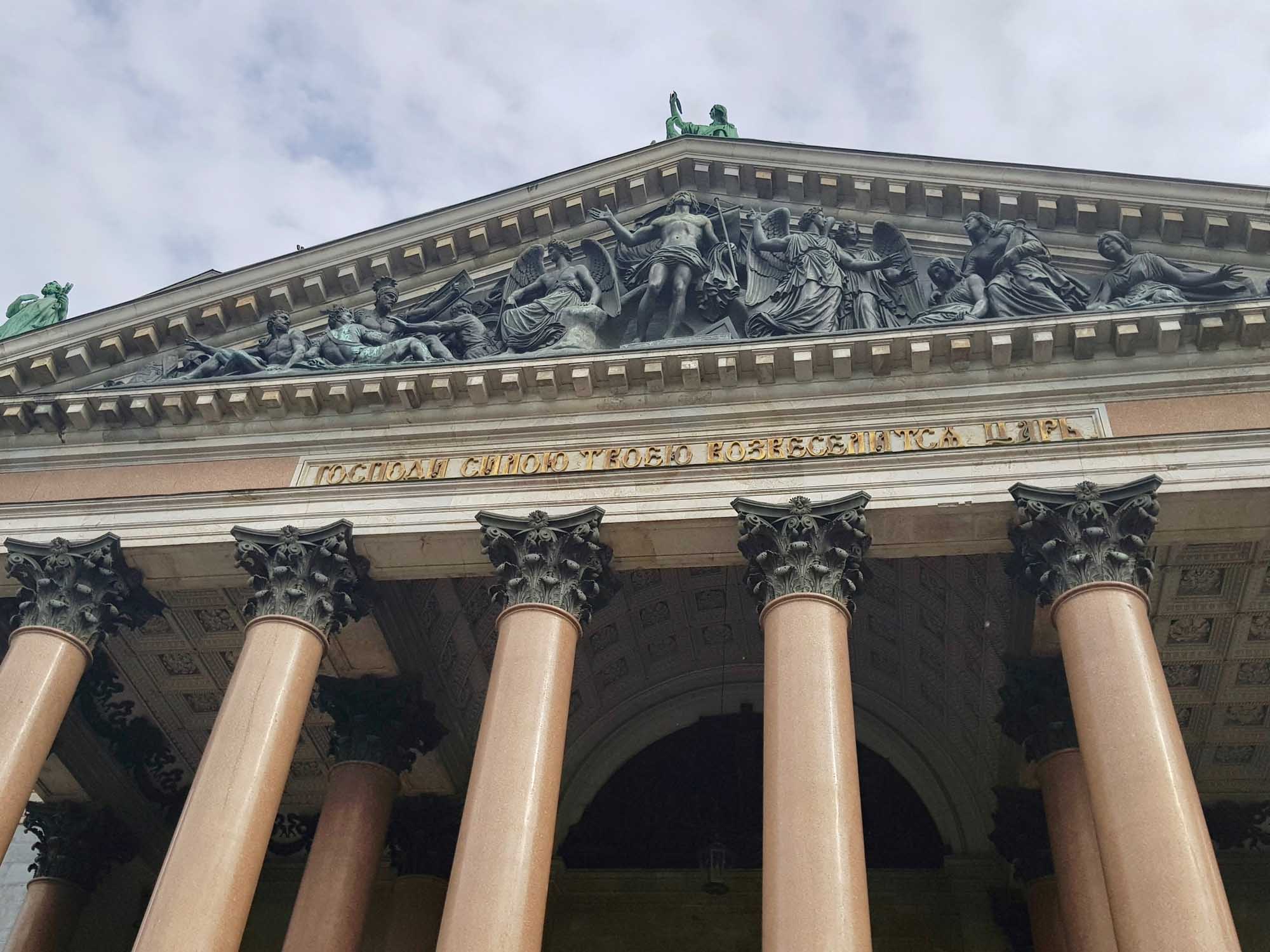 Classical Neoclassical Building with Corinthian Columns A striking neoclassical facade featuring six tall Corinthian columns with ornate capitals supporting an elaborate pediment adorned with classical sculptural reliefs. The building displays characteristic Beaux-Arts architecture with detailed stonework and Cyrillic inscription text visible above the colonnade.