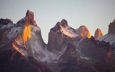 Dramatic Mountain Peaks at Golden Hour Towering granite peaks bathed in warm golden and orange light during sunset or sunrise, with snow and ice visible on the upper slopes and dramatic shadows creating depth across the jagged mountain range.