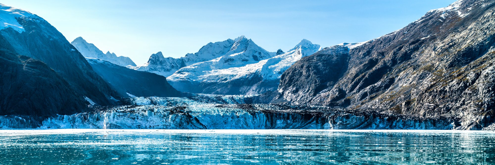 Glacier Bay Tidewater Glacier and Mountain Valley A stunning glacial landscape featuring a massive tidewater glacier flowing between snow-capped peaks into a turquoise-blue glacial lake, surrounded by steep mountain cliffs and rocky terrain under clear skies.