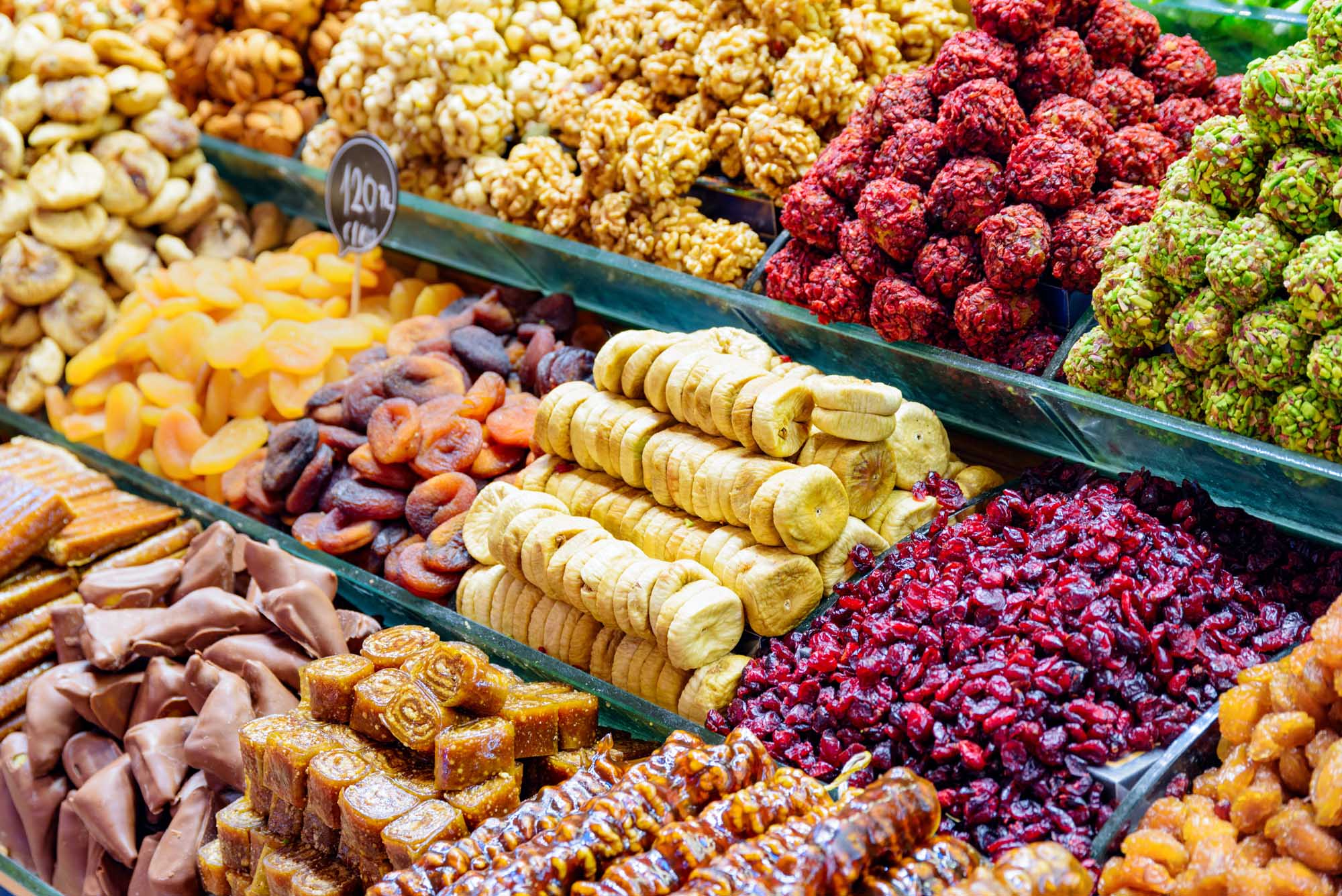 Grand Bazaar Sweet Display in Istanbul A vibrant display of traditional Turkish sweets and dried fruits at the Grand Bazaar in Istanbul. The market stall showcases an array of colorful confections including baklava, dried apricots, banana chips, fresh raspberries, mulberries, and various wrapped candies arranged in green display trays, representing the rich culinary heritage of this historic marketplace.