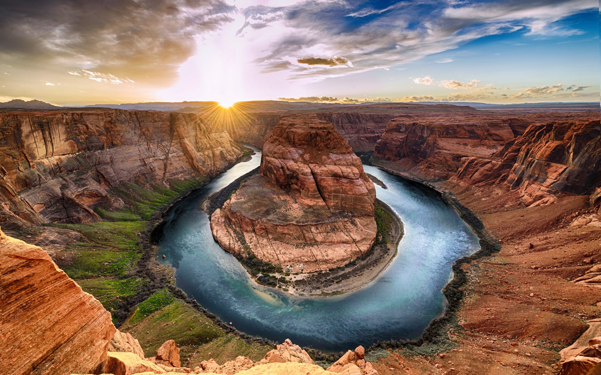 Horseshoe Bend Colorado River Sunset A breathtaking aerial view of Horseshoe Bend, where the Colorado River makes a dramatic 270-degree horseshoe-shaped meander through towering red sandstone cliffs. The scene captures the turquoise river snaking through the desert landscape during golden hour, with vibrant blue sky and puffy clouds creating a stunning contrast against the warm, rust-colored canyon walls.