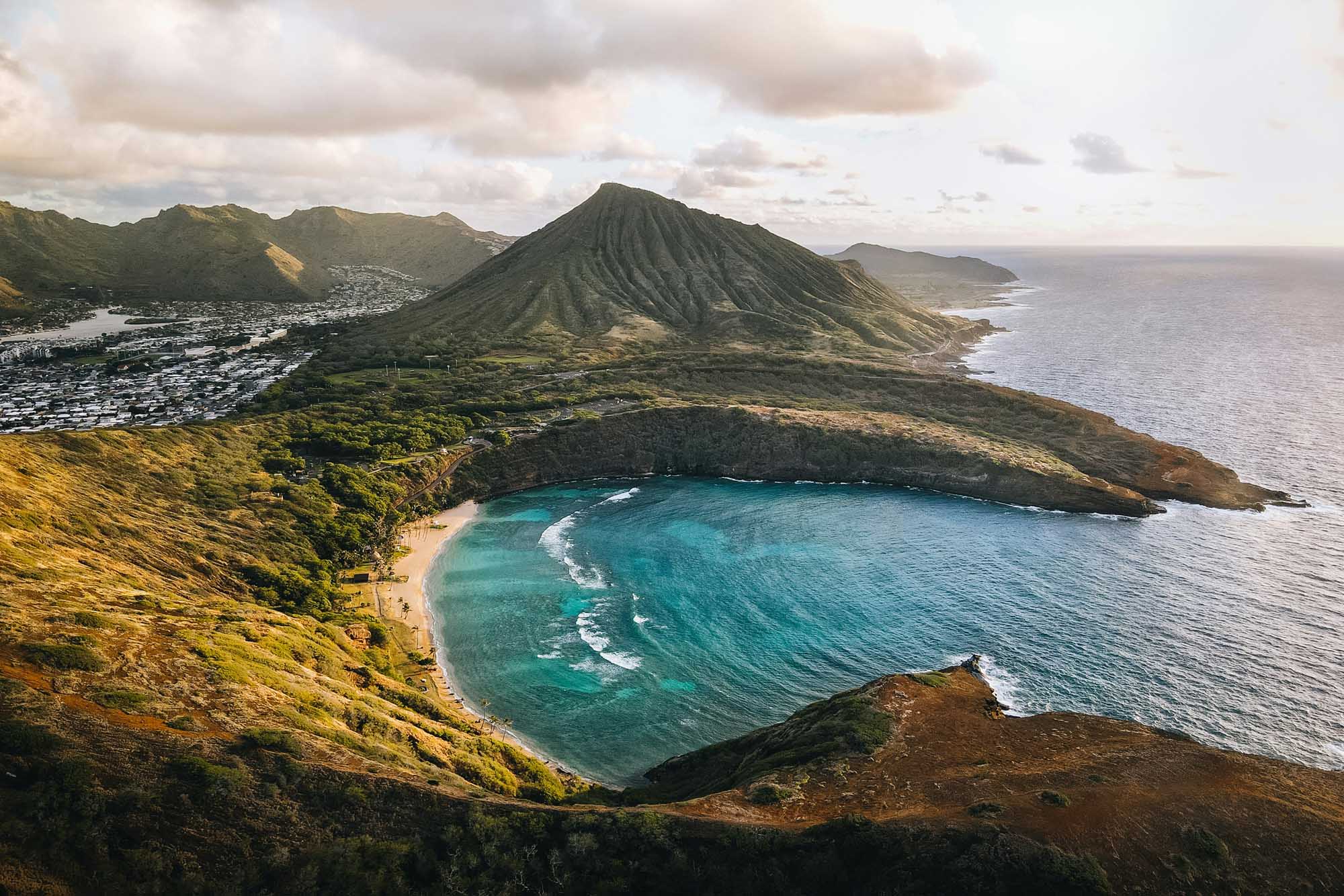 Koko Crater Bay with Volcanic Peak, Hawaii A stunning aerial view of Koko Crater and Koko Head in Hawaii, featuring a pristine turquoise bay with white sand beach nestled between dramatic volcanic ridges, with the iconic conical peak rising prominently in the background and a coastal town visible along the shoreline.