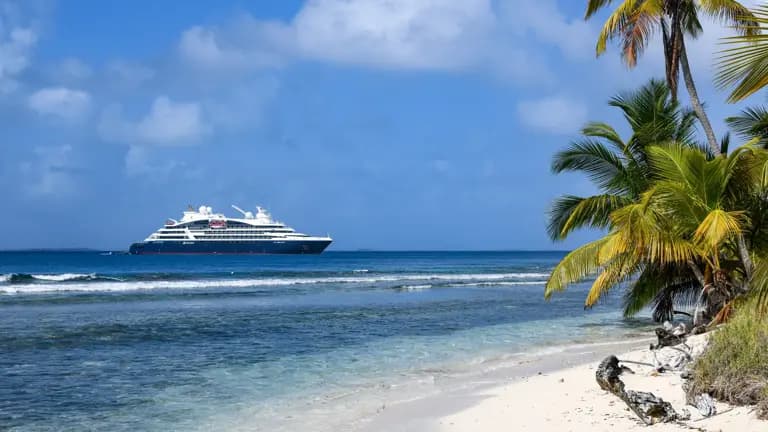 Luxury Cruise Ship Anchored Off Tropical Beach A large modern cruise ship anchors in clear turquoise waters off a pristine tropical beach lined with palm trees, exemplifying a classic Caribbean or Central American cruise destination with white sand, calm waters, and lush vegetation.